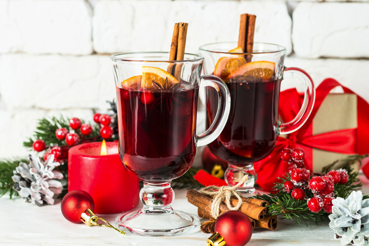 Glühwein im Glasbecher mit Frucht und Gewürzen auf Weiß